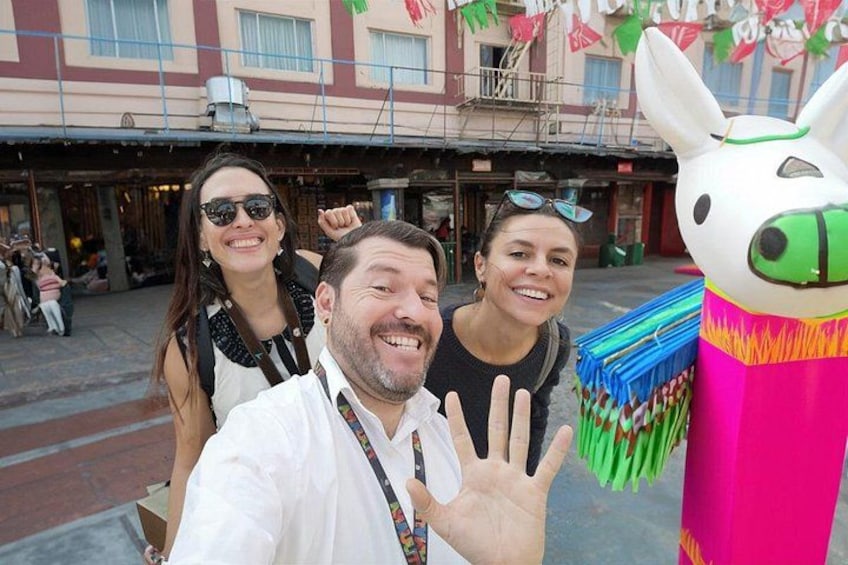 Three people taking a selfie with a colorful inflatable llama in an urban street setting. 2