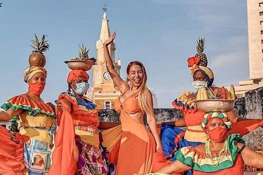 Eine Gruppe von Menschen in farbenfroher traditioneller Kleidung, im Hintergrund ein Glockenturm. 1