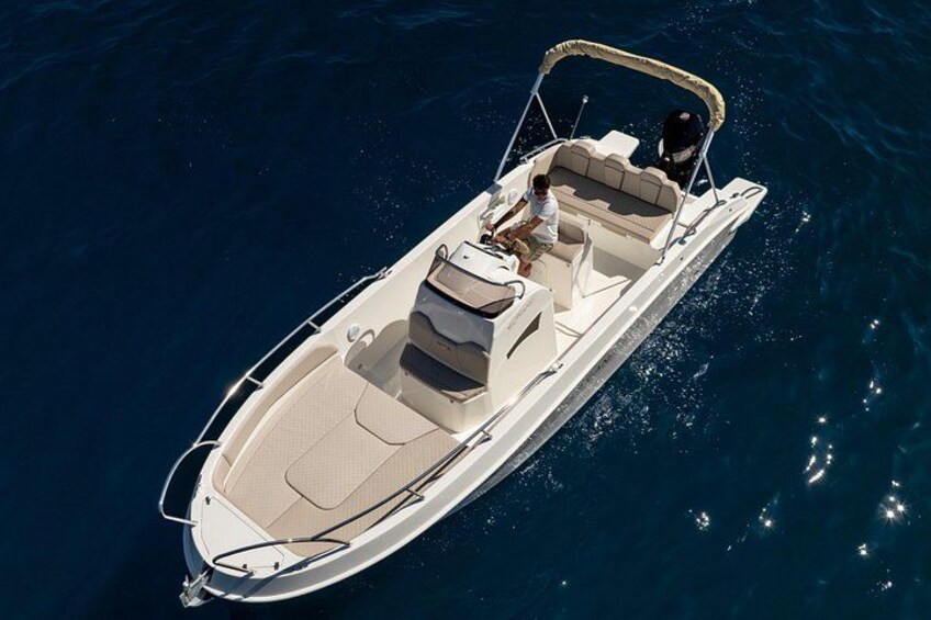 A white motorboat with a canopy, two passengers, and a wake behind it. 1