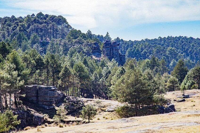 A mountainous landscape with dense forests, rocky outcrops, and a prominent cliff face. 5