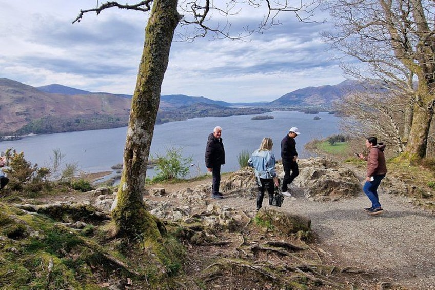 A group of people standing on a rocky path overlooking a lake with mountains in the background. 3