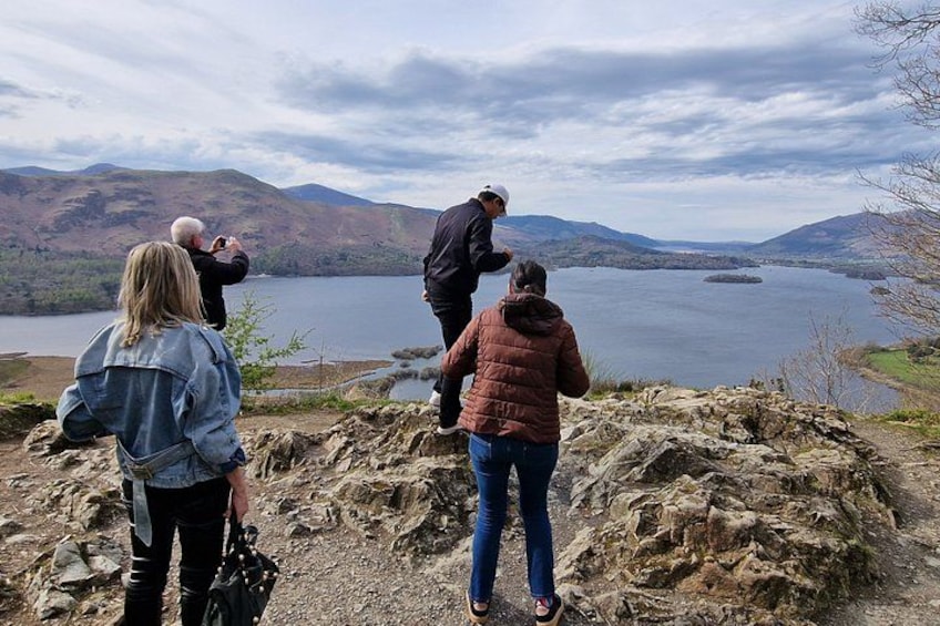 A group of people standing on a rocky outcrop overlooking a lake with mountains in the background. 2