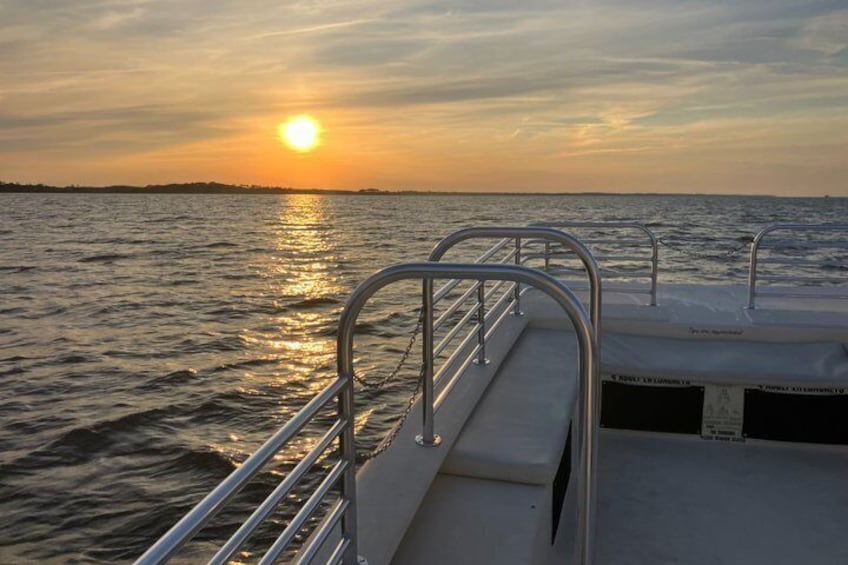 A boat deck with metal railings and a view of the sunset over the water. 3