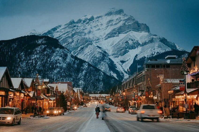 A snow-covered mountain town street at dusk with buildings and cars. 3