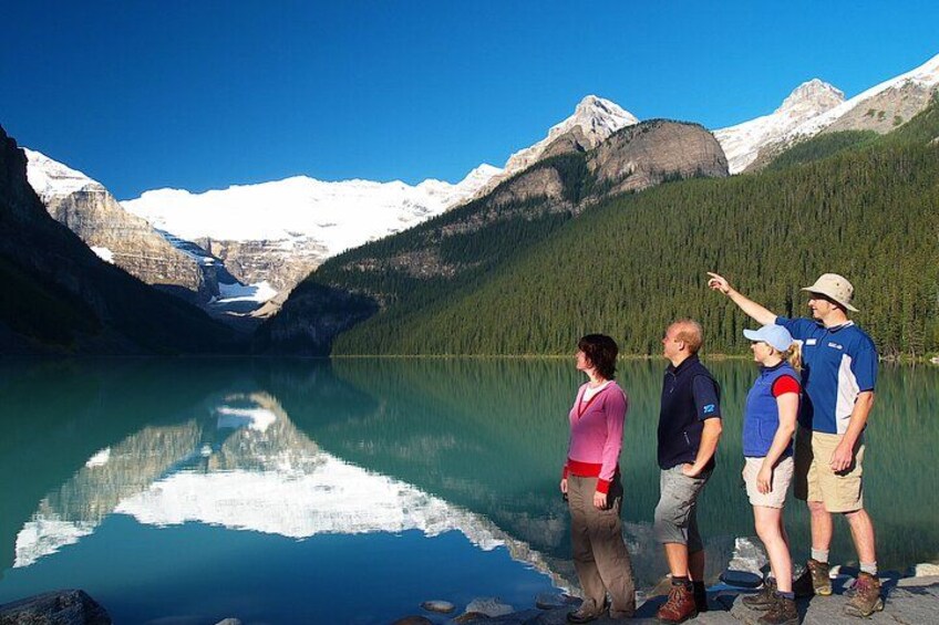 Eine Gruppe von Menschen steht an einem ruhigen See, im Hintergrund sind Berge zu sehen. 4