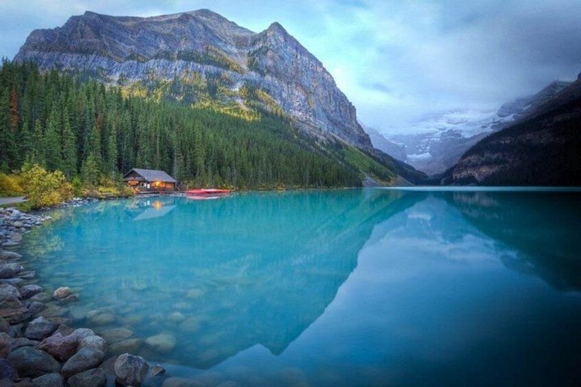 A lake with clear turquoise water, surrounded by forested mountains and a cabin. 5