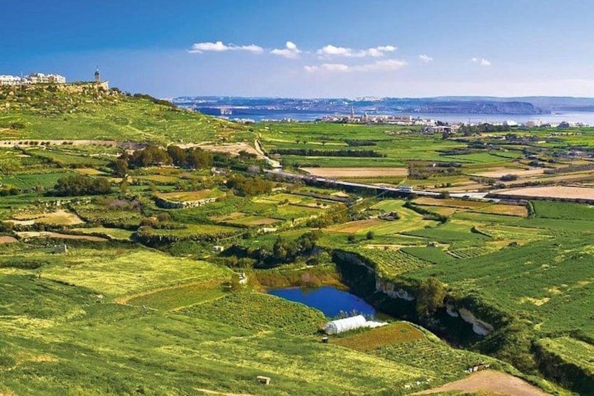 Paisaje costero con colinas ondulantes, una extensión de agua y edificios a la distancia. 4