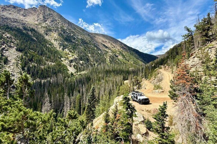 A jeep on a dirt road in a forested mountainous area. 1