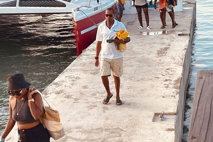 A pier with people walking, a boat docked, and a sandy surface. 5