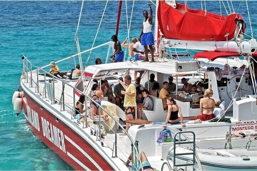 A crowded boat with people standing and sitting, sailing on clear blue water. 1