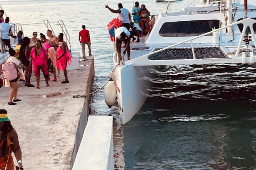 A group of people on a dock by a boat, with water and a boat's hull visible. 4