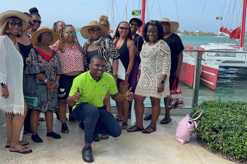 A group of people posing by a waterfront with boats and a flag in the background. 5