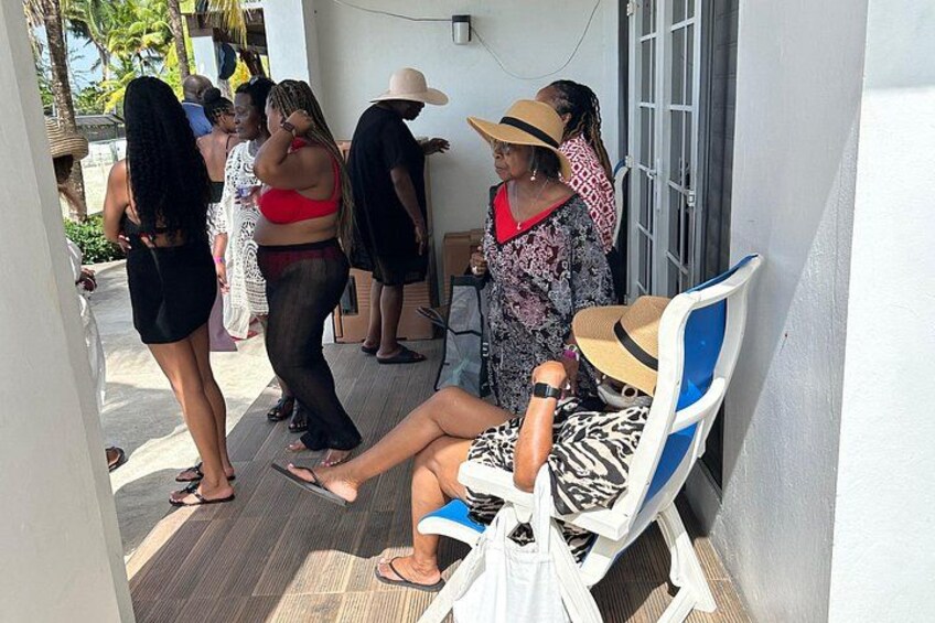 A group of people standing and sitting on a porch, some wearing hats and others in casual clothing. 2