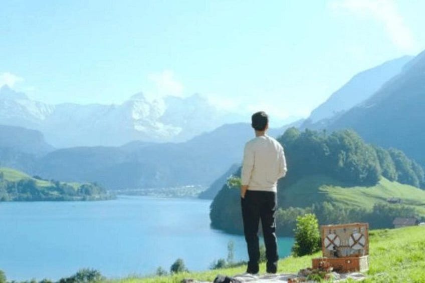 Un hombre está de pie sobre una colina cubierta de hierba, con vistas a un lago y montañas al fondo. 4