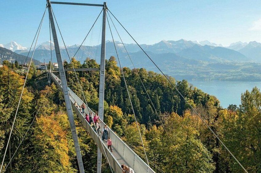 Un puente colgante con gente caminando, rodeado de bosque y montañas. 3