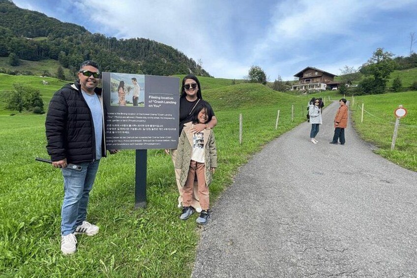 Una familia de pie junto a un cartel en un entorno rural, con una casa al fondo. 5