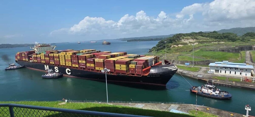 A large cargo ship with multiple containers, docked at a port with a small tugboat nearby. 4