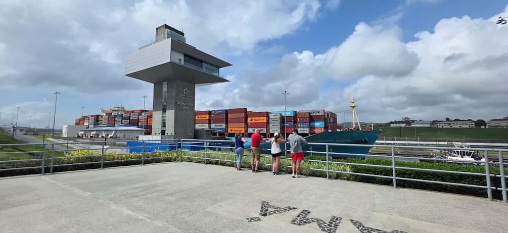 A port with shipping containers, a large blue ship, and a modern building with a tower. 2