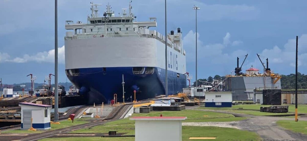 A large ship docked at a port with cranes and construction equipment nearby. 3