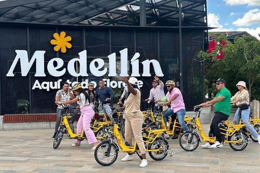 A group of people on bicycles in front of a building with a sign that reads 'Medellin.' 5