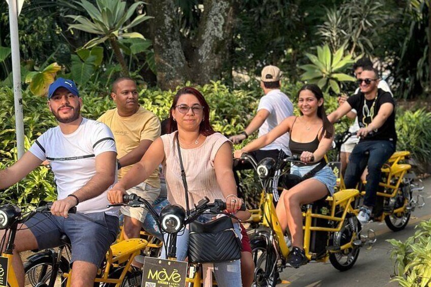 A group of people riding bicycles on a paved path surrounded by greenery. 1