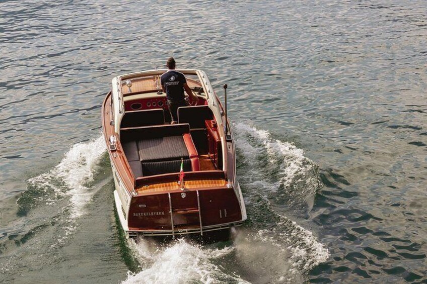 A wooden motorboat with a person steering, moving through calm water. 4
