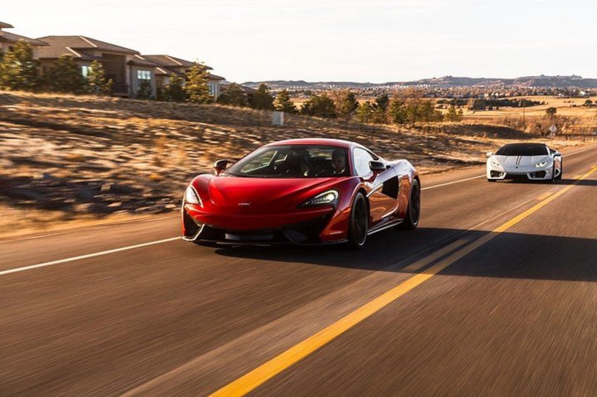 A red sports car driving on a road with a white sports car following. 2
