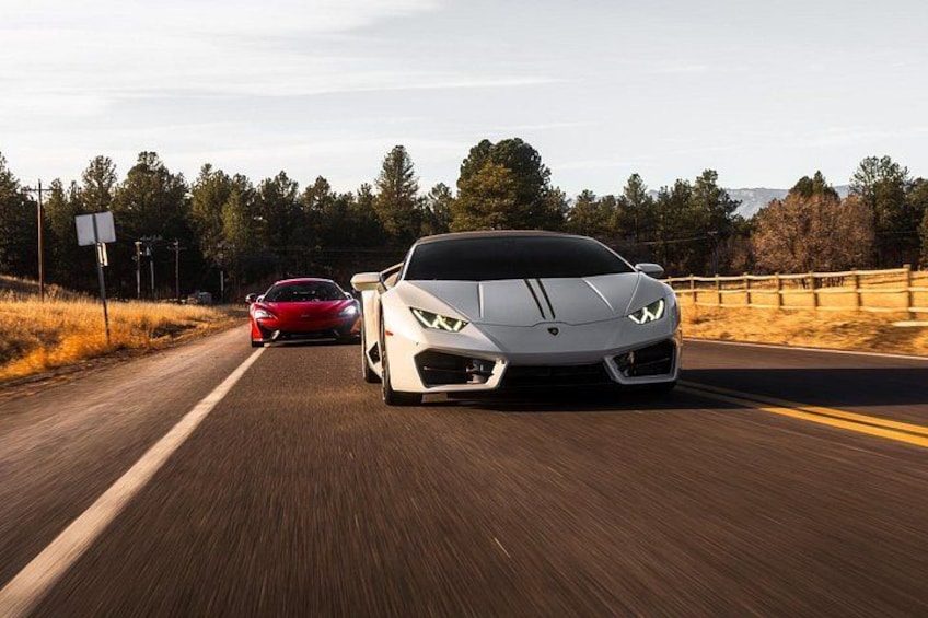 A white sports car driving on a road with a red car ahead, surrounded by trees and a clear sky. 4