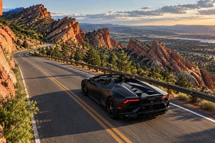 A black sports car driving on a winding mountain road with rocky terrain and a view of a valley. 3