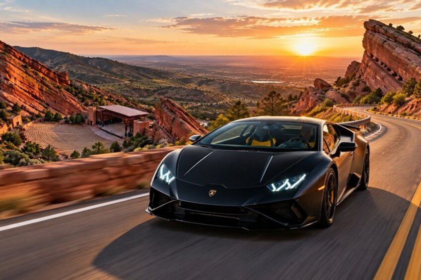A black sports car driving on a winding road with a scenic sunset and rocky landscape in the background. 2