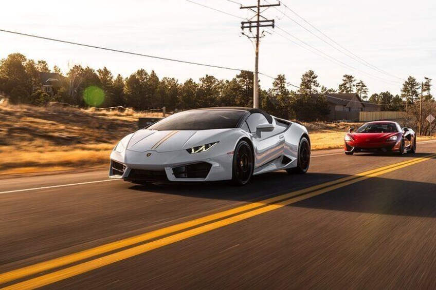 A white sports car driving on a road with a red sports car in the background. 1