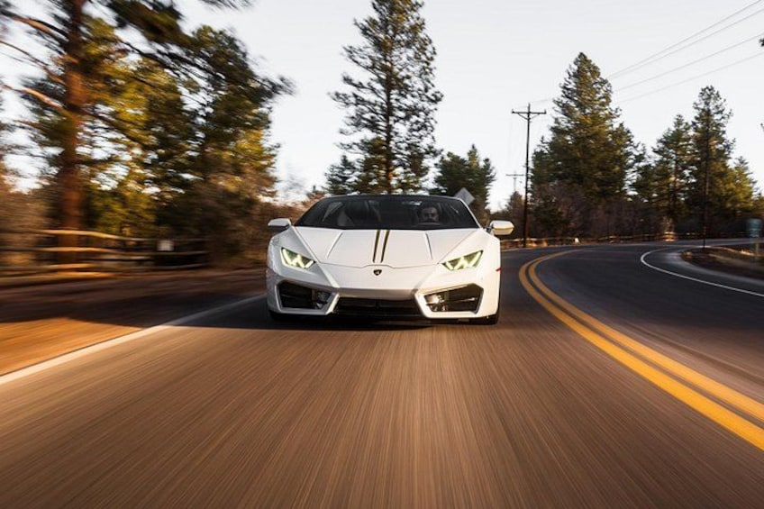 A white sports car driving on a road with trees on the side. 3