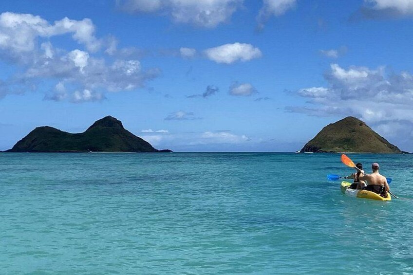 A kayak on calm turquoise water with two green islands in the background. 1
