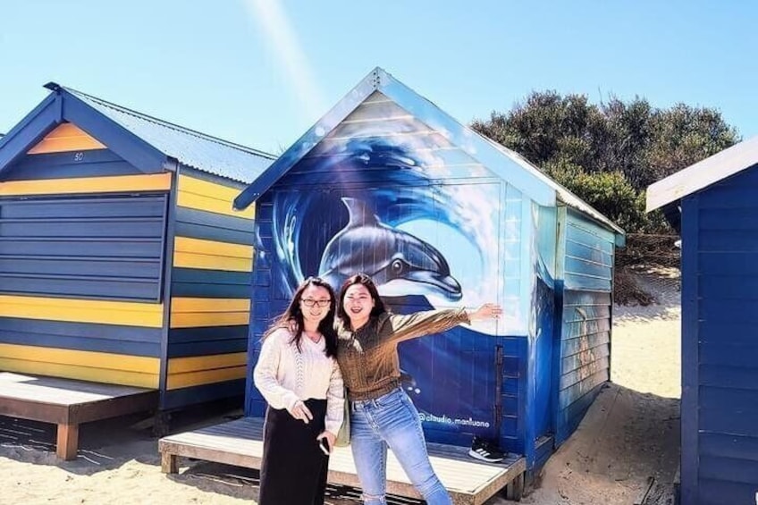 A beach with a blue and yellow beach hut and a mural of a dolphin. 1