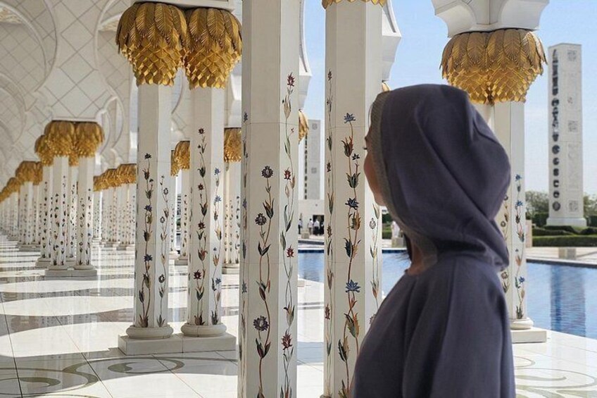 Une personne vêtue de bleu se tient dans un vaste hall orné de colonnes blanches et d’éléments décoratifs dorés. 3