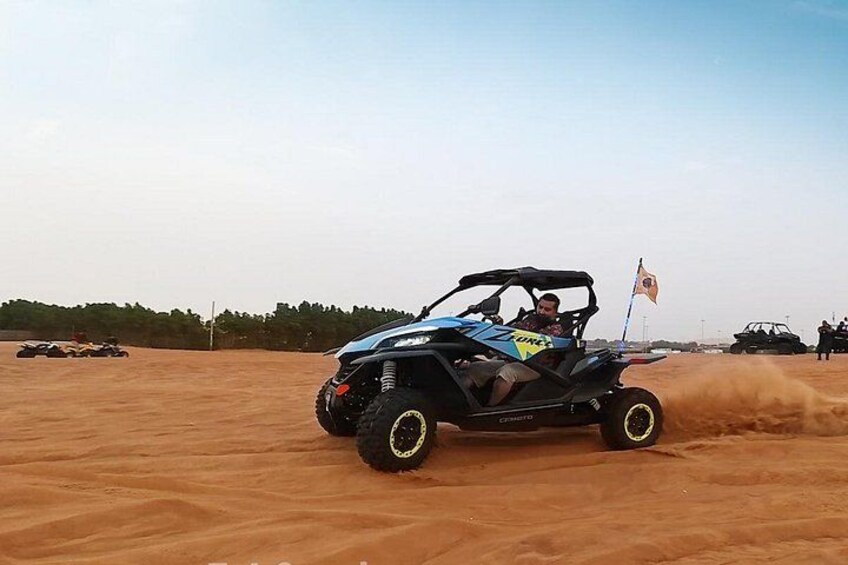 A person driving a black off-road vehicle on a sandy terrain with other vehicles in the background. 2