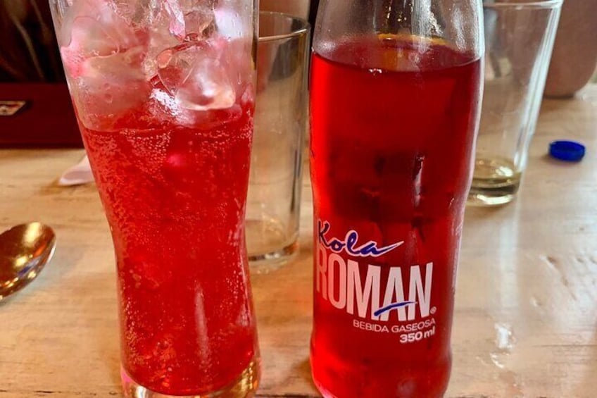 Un vaso de bebida roja con cubitos de hielo y una botella etiquetada como 'Cola Roman' con un volumen de 350 ml. 1