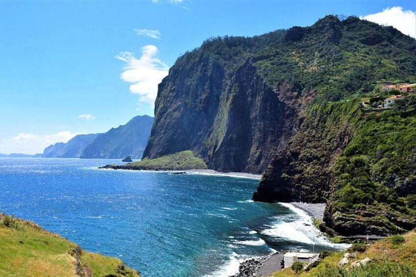 A coastal landscape with steep cliffs, a clear blue sea, and a small settlement on the hillside. 4
