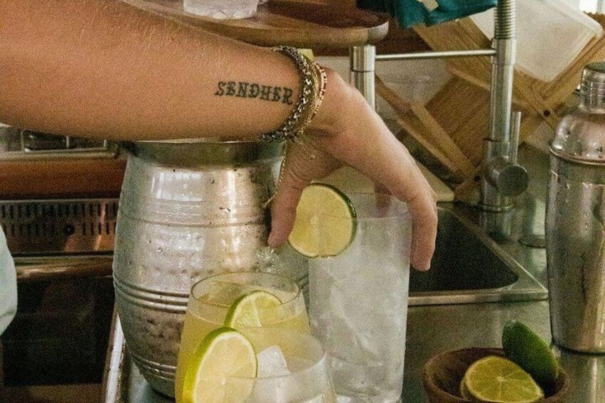 A person pouring a drink from a metal container into a glass with ice and lime slices. 1