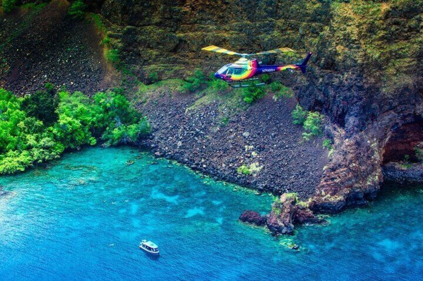 A helicopter flying over a coastal area with clear turquoise water and rocky cliffs. 1