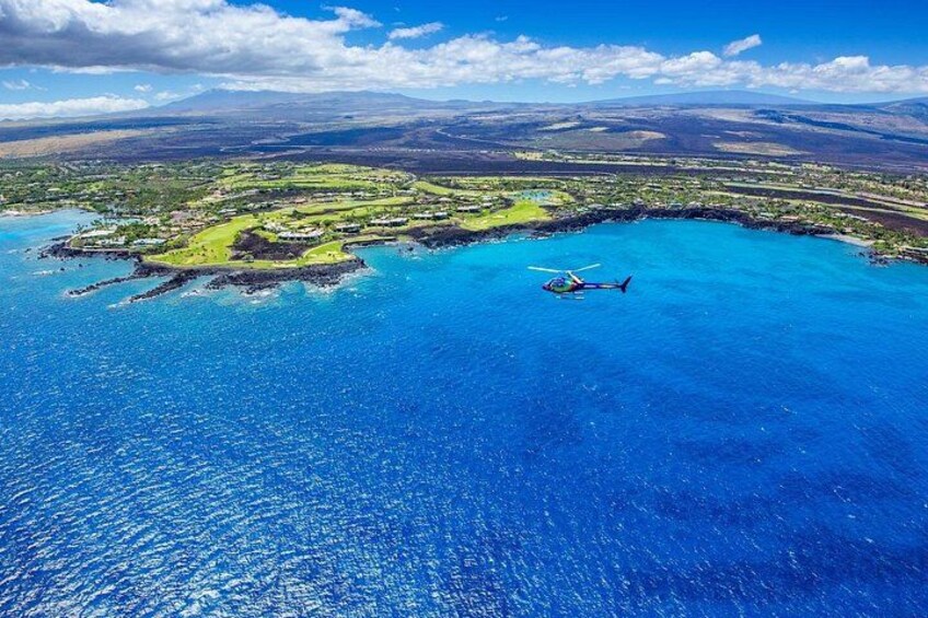 An aerial view of a coastal area with a helicopter, clear blue waters, and a green landscape. 3