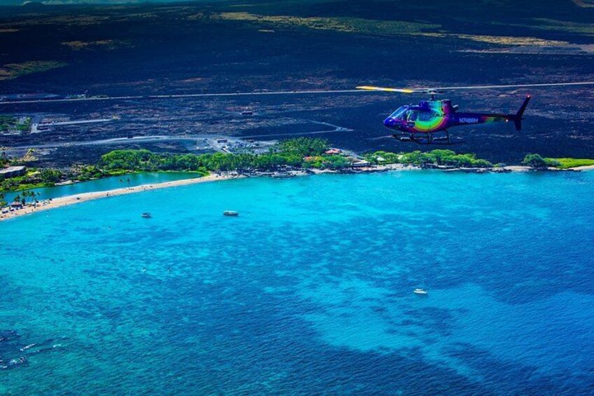 A helicopter over a coastal area with clear blue waters, a beach, and a small island. 4