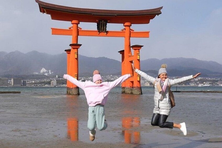 Two people jumping in front of a red torii gate with mountains in the background. 2