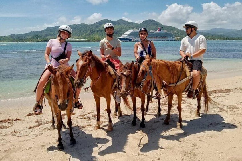 Quattro persone cavalcano cavalli su una spiaggia con una nave da crociera sullo sfondo. 1