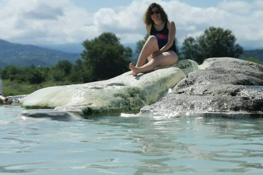 A person sitting on a rock by a clear water body with mountains in the background. 1