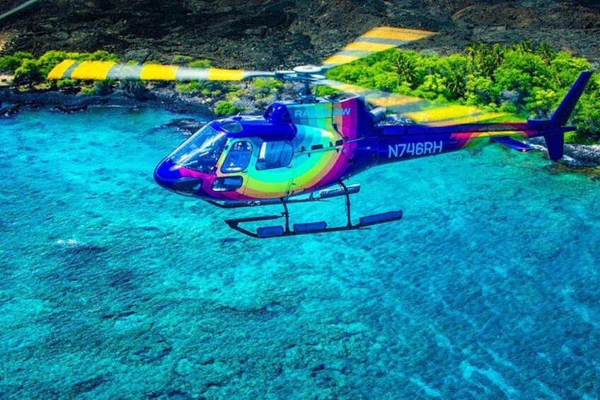 A helicopter with registration N746RH flying over a clear blue sea with a tropical landscape in the background. 5