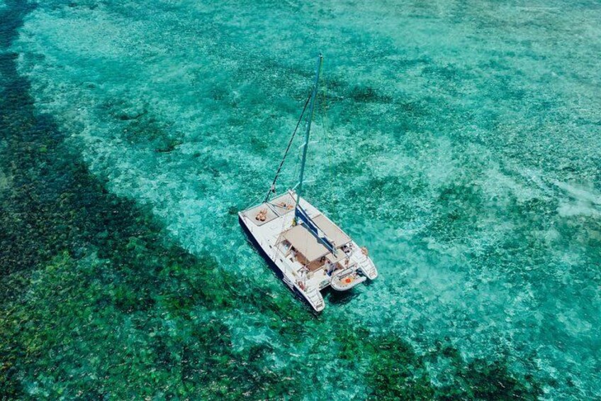 A white boat with a cabin and a mast, floating on clear turquoise water. 4