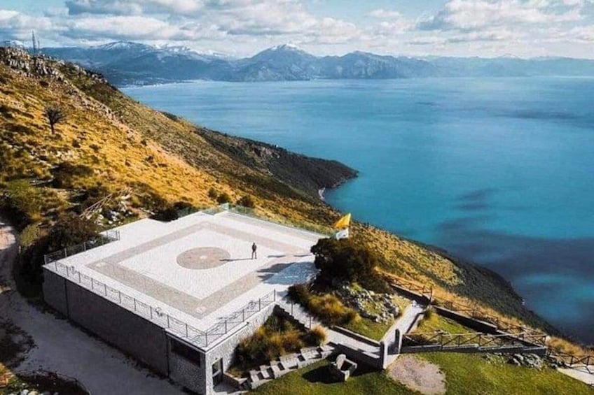 A large building with a circular courtyard, surrounded by a hilly landscape and a body of water. 1