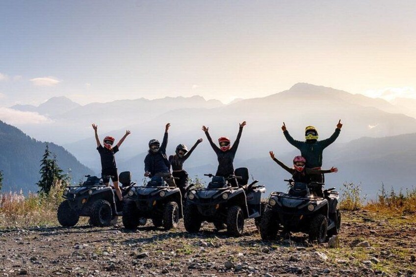 Four people on ATVs with their arms raised, standing on a rocky terrain with mountains in the background. 5