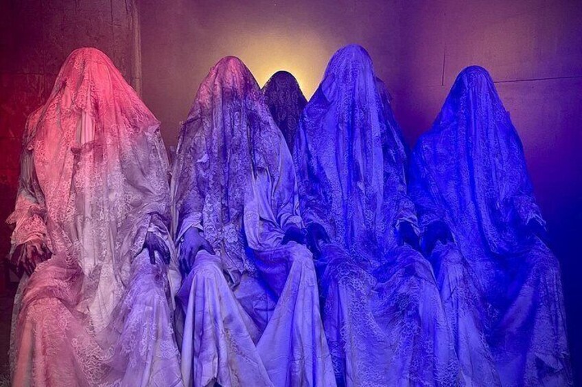 Un grupo de personas vestidas con prendas fluidas y translúcidas, sentadas en fila. 5